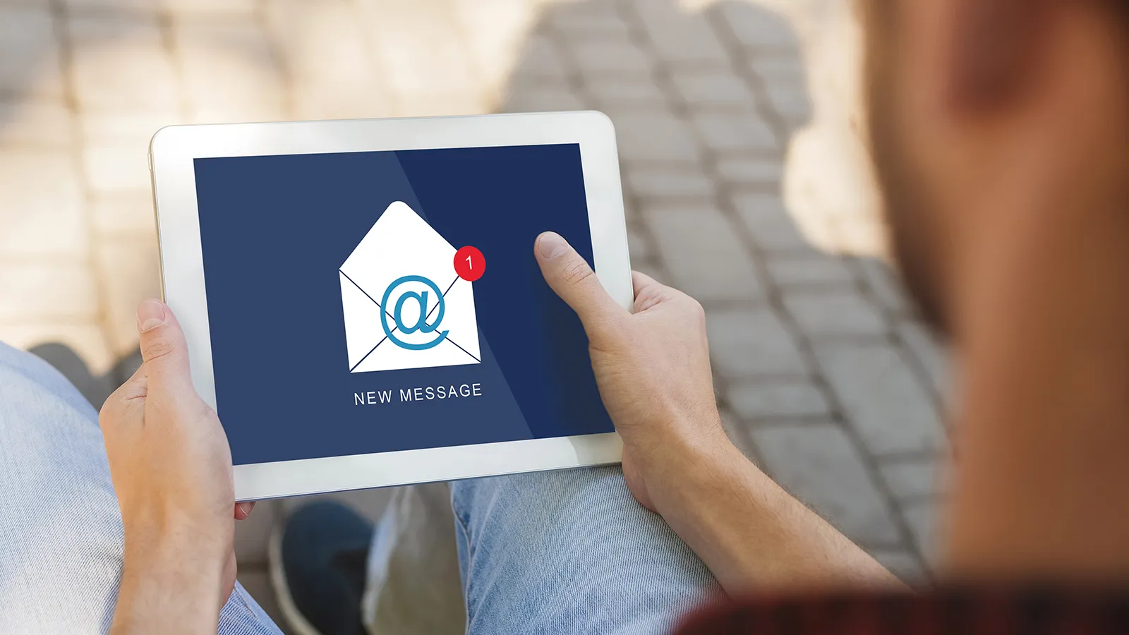 a male holding a tablet that has the text "new message" on it and an illustration of an envelope with an ampersand and red circle with a number 1 on it