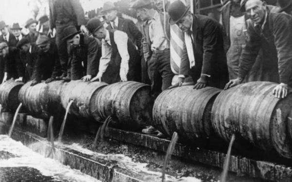 men dumping alcohol from large barrels into the street